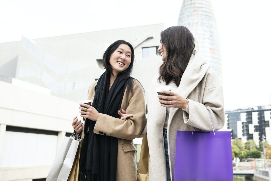 two happy beautiful girls shopping in the city with shopping bags and cup of coffee - fashion and