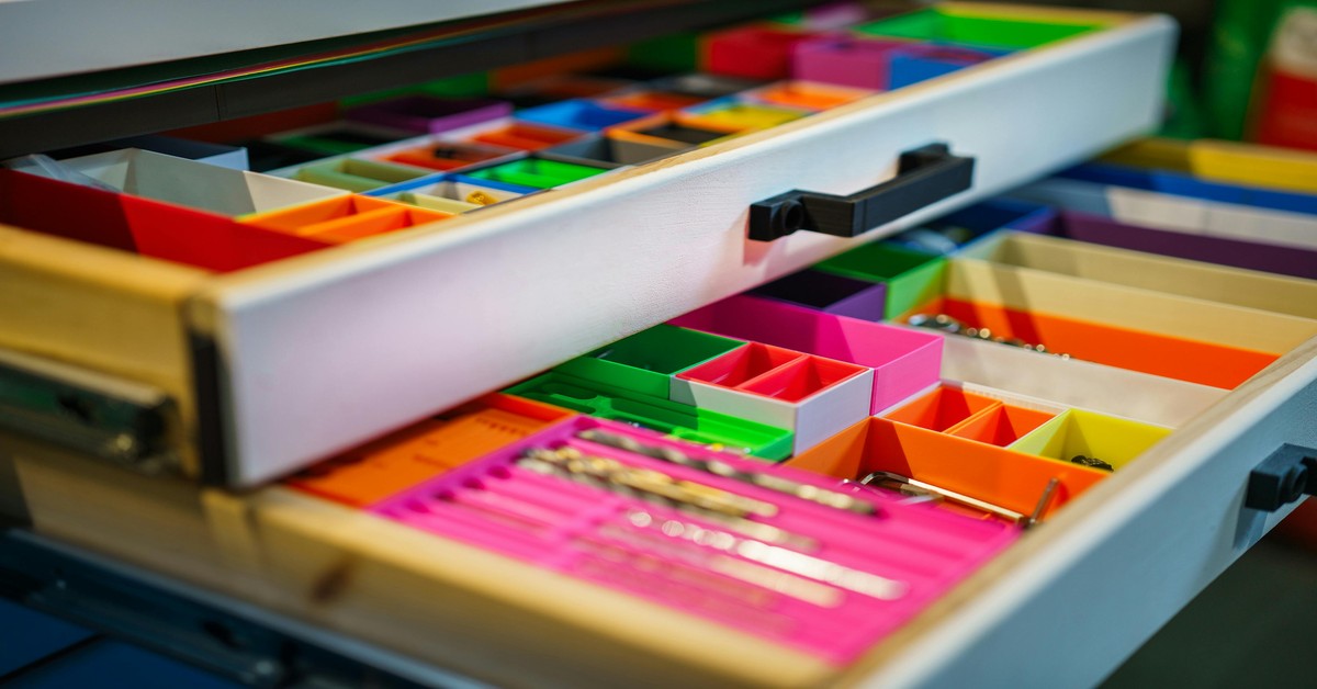 Several 3D printed drawer organizers neatly arranged in a desk drawer, showcasing different sizes and colors