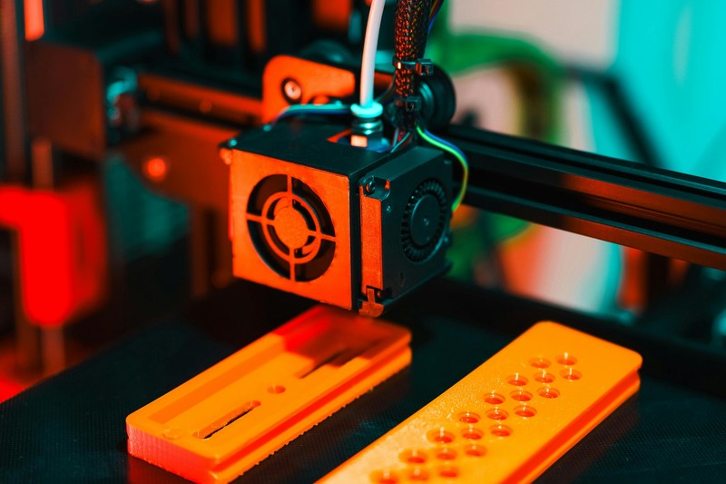 A collection of 3D printer accessories including spare nozzles, digital calipers, and a glue stick arranged on a workbench.