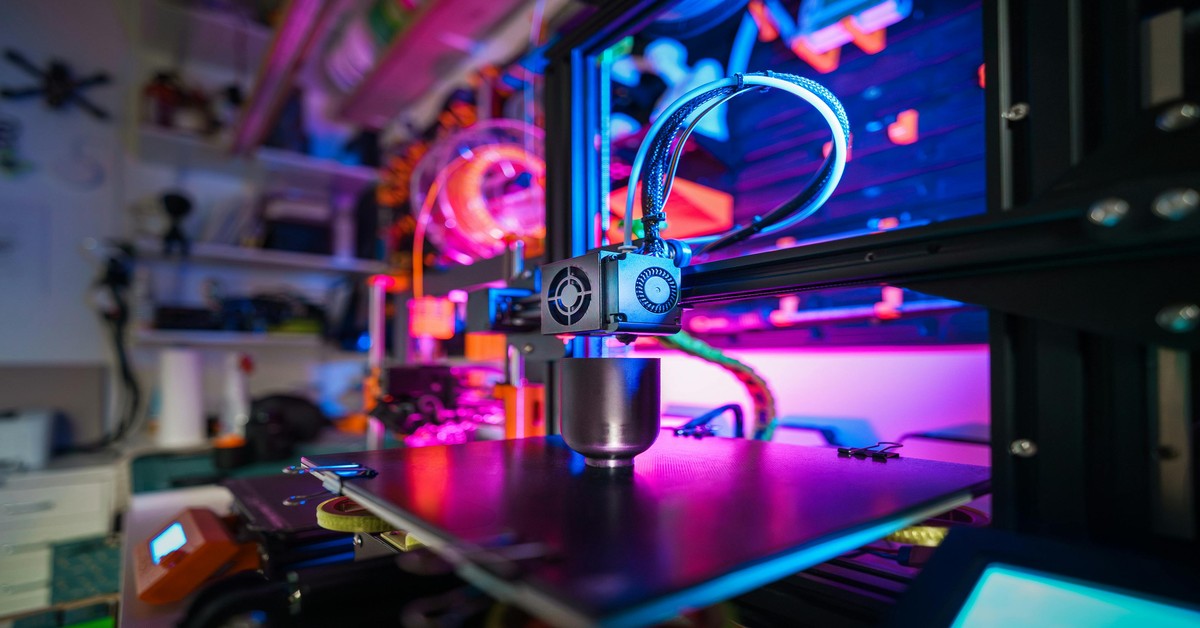 A desktop 3D printer printing a plastic prototype on a workbench in a workshop