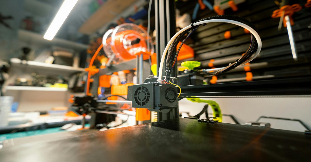 FDM 3D printer printing a mechanical part with orange filament on a build plate