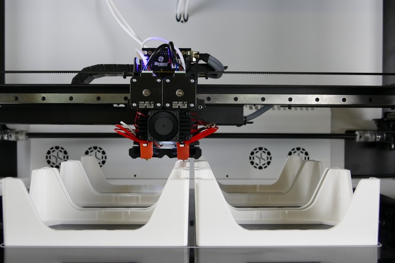 A large industrial 3D printer with an enclosure printing a nylon part