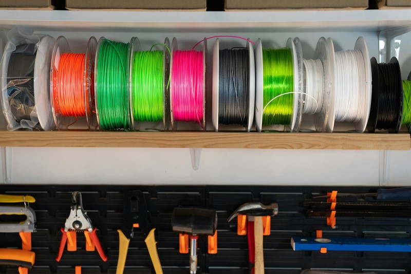 A spool of white PLA filament next to a 3D printer